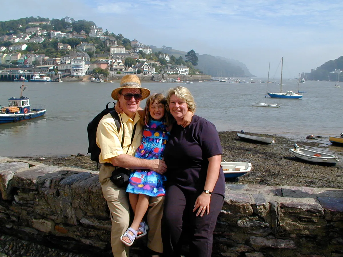 Cassandra as a young girl with her forever family, sitting on a harbour wall by the water